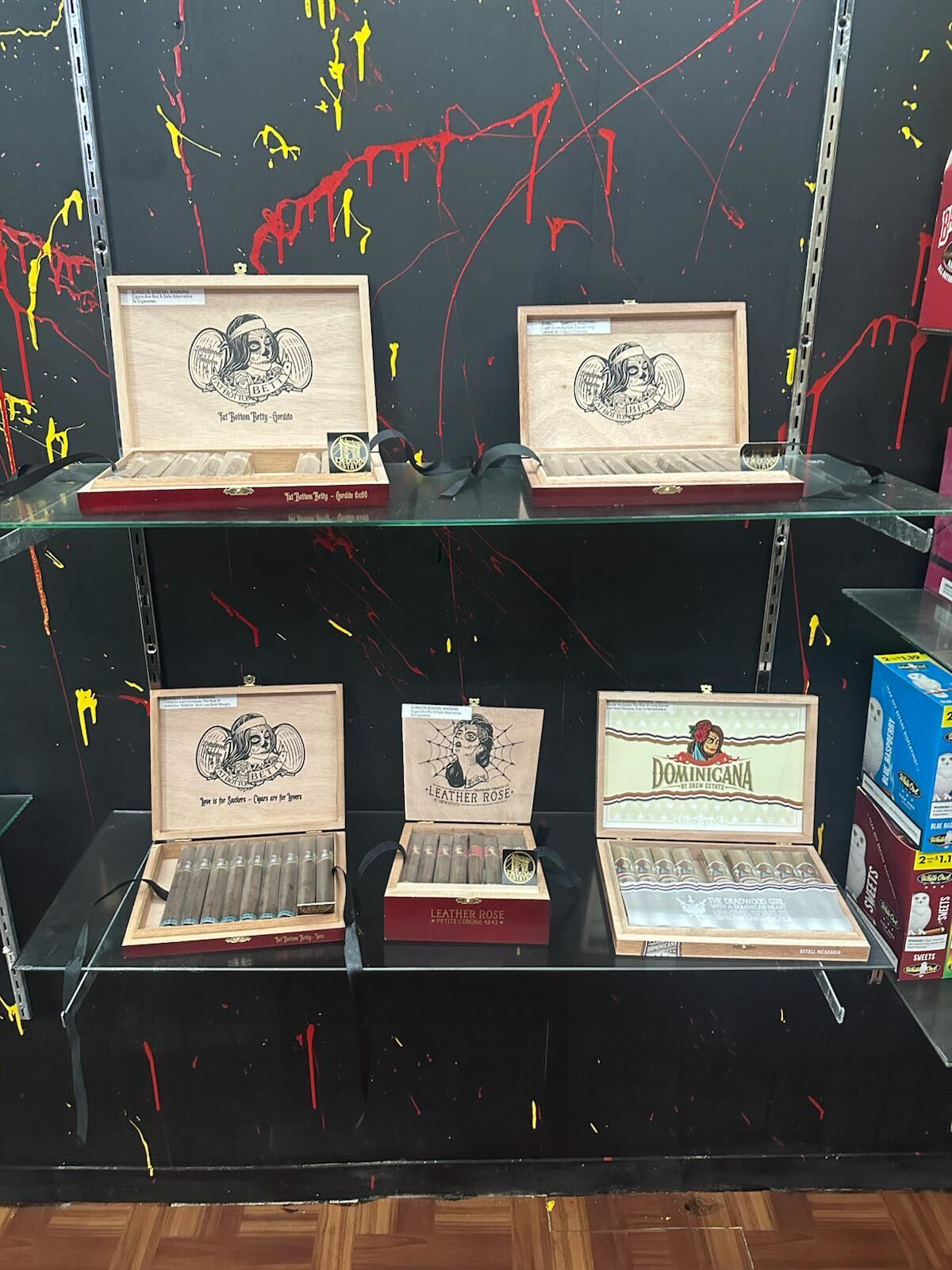 Cigar boxes displayed on glass shelves with colorful paint splatters background